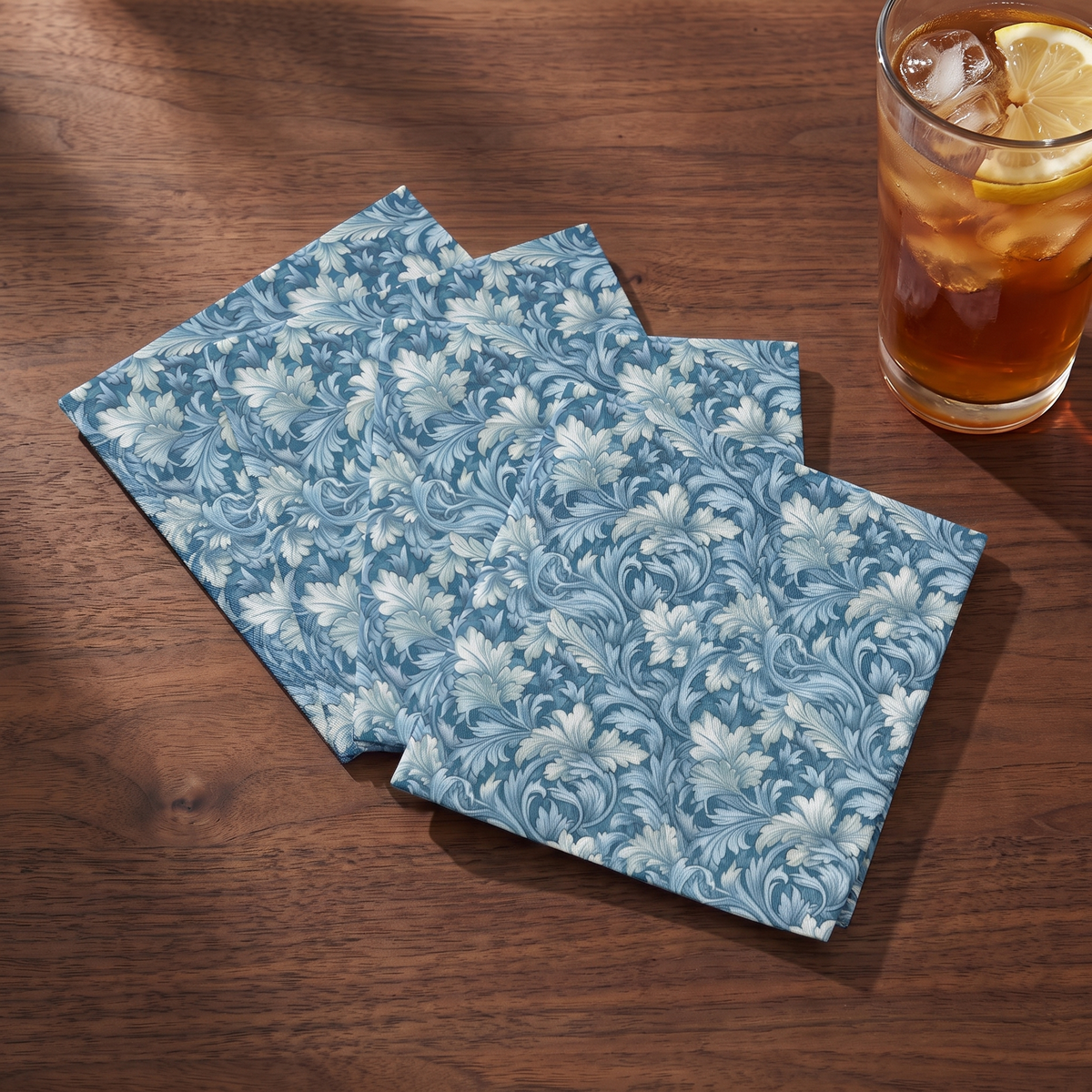 Soft Blue Leaf Tapestry cocktail napkins beside an iced drink on walnut wood