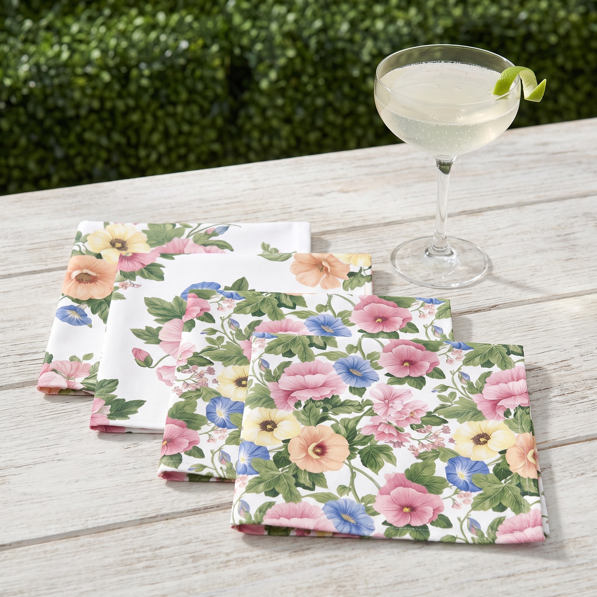 Four Pastel Garden Elegance cocktail napkins beside a coupe cocktail on a garden table