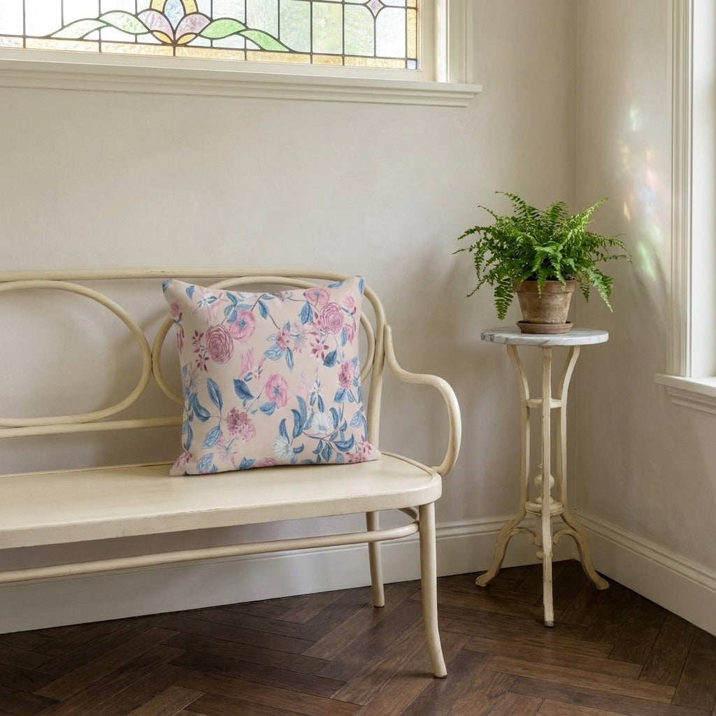 Blush Bloom Serenity square throw pillow on a pale curved bench in a sunlit room