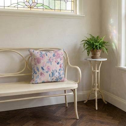 Blush Bloom Serenity square throw pillow on a pale curved bench in a sunlit room