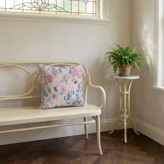 Blush Bloom Serenity square throw pillow on a pale curved bench in a sunlit room